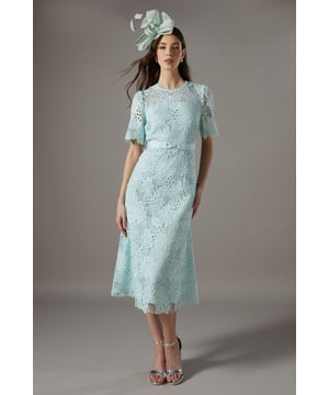 Exquisite lace midi dress with intricate floral pattern
        Elegant bow belt accentuates the waistline
        Flattering round neckline and short sleeves
        Scalloped hem adds a delicate touch
        Midi length perfect for formal occasions
    
    This stunning lace midi dress radiates sophistication and grace, making it an ideal choice for weddings, races, or any formal event where you want to make a lasting impression. The intricate floral lace pattern adorns the entire dress, creating a romantic and feminine silhouette. The bow belt cinches the waist beautifully, enhancing your figure and adding a charming detail. Style this dress with a matching fascinator, as shown, for a coordinated look that's sure to turn heads. Pair with strappy metallic heels and a clutch bag to complete your ensemble. For cooler evenings, drape a lightweight pashmina over your shoulders. This versatile piece can be dressed up or down, making it a valuable addition to your occasion wear wardrobe.