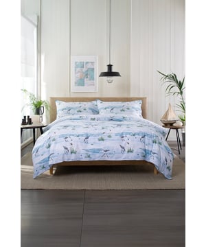 Capturing a serene shoreline scene, Waders features delicate illustrations of coastal birds foraging along the water’s edge. The design uses muted blues, greens, and sandy tones to reflect the calm beauty of nature. Crafted from 100% cotton with a 144-thread count, this bedding set is completed with a piped finish and a coordinating printed fabric bag.