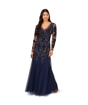 Luxe beading and velvet are in full bloom throughout this mermaid gown. This formal dress features a v-neckline flanked by inset sheer panels, sheer long sleeves, and a mermaid skirt with godet skirt. Crafted from knit mesh, this long sleeve gown is embellished with sequin and beaded florals accented with rich velvet through the mid-skirt. A zipper closure at the centre back completes this evening gown. Styled with neutral heels and a contrasting clutch, this long sleeve gown makes every night more elegant.