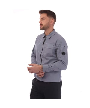 Mens C.P. Company Organic Gabardine Full-Zip Overshirt in lavender.- Classic collar.- Full zip fastening.- Chest flap snap pocket.- Adjustable button cuffs.- Lens detail.- Garment dyed.- Regular fit.- 100% Cotton.- Ref: 18CMOS124A774