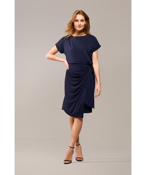 De navy Riley rok van Mart Visser is de ideale mix van casual en sportief, en biedt tegelijkertijd een elegante uitstraling. Met een flatterende lengte die net boven de knie valt, is de rok gemaakt van een hoogwaardige jersey stof die ultiem comfort biedt. De lichte stretch in de stof zorgt ervoor dat de rok soepel om je lichaam valt, waardoor het je favoriete rok zal worden. De donkerblauwe overslagrok heeft een asymmetrisch strikdetail aan de linkerzijde, wat zorgt voor een bijzonder effect. Het rechte model heeft een elastische tailleband aan de achterkant voor de perfecte pasvorm en comfort. De Riley rok benadrukt zowel draagbaarheid als stijl. Combineer de navy rok met de bijpassende Raist top voor een elegante jurk-look, en maak de look af met een mooie blazer en zwarte laarsjes. Ga voor een comfortabele, maar chique uitstraling!