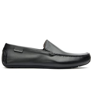 Zapatos moteros Cole Haan negros para hombre, fabricados en piel y suela de goma. Incluyen refuerzo lateral elástico, logo de Cole Haan, piel suave, plantilla acolchada y suela motera.