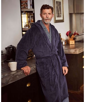 Our popular navy fleece dressing gown has been updated with a cosy hood. Lightweight yet beautifully soft and warm, it's complete with two handy patch pockets and a loop at the back of the neck for hanging. 100% Polyester super soft polyester. 260 gms light weight but super warm and toasty. Deep hooded. 2 patch pockets. Length 117cm approx. Back neck hanging loop. Machine washable at 40°C. Model is 6ft 2" and wears size M.