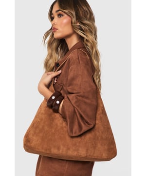 Textured faux suede finish with a soft-touch feel
        Spacious main compartment for all your essentials
        Sleek hobo silhouette with minimalist design
        Single shoulder strap for comfortable carrying
        Secure magnetic button closure to keep belongings safe
    
    This structured faux suede tote bag combines practicality with effortless style. The minimalist design makes it a versatile addition to your accessories collection, whilst the roomy interior provides ample space for daily essentials. Style with coordinating outerwear as seen on our model for a cohesive look, or contrast with denim and a crisp white shirt for casual daytime outings. The neutral tone works beautifully for family gatherings or coffee dates, pairing perfectly with flat shoes and relaxed silhouettes. For a touch of polish, match with tailored trousers and a fine knit jumper. This Boohoo bag transitions seamlessly from day to evening, making it an indispensable companion for the fashion-forward woman who values both style and functionality.