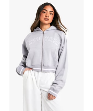 Cropped design for a trendy silhouette
        Full-length zip closure for versatile styling
        Bold 'New York' slogan across the chest
        '06' detail on the sleeve for a sporty touch
        Comfortable hood for added warmth and style
    
    Make a statement with this eye-catching cropped hoodie, perfect for the fashion-forward trendsetter. The bold 'New York' slogan and '06' detail give it an urban, street-style edge that's sure to turn heads. Its versatile design allows for effortless styling - pair it with high-waisted trousers and trainers for a casual daytime look, or throw it over a bodycon dress for an edgy night out ensemble. The full-length zip offers adaptability, allowing you to customise your look to suit the occasion or weather. Ideal for everything from coffee dates to weekend shopping trips, this hoodie is a must-have addition to any casual wardrobe. Its cosy hood and soft fabric ensure comfort without compromising on style, making it the perfect go-to piece for those days when you want to look effortlessly cool.