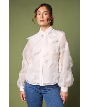 Exquisite organza blouse adorned with striking 3D flower appliqus
        Elegant collared neckline with feminine pussy bow detail
        Voluminous balloon sleeves for dramatic silhouette
        Semi-sheer finish with lined body for sophisticated coverage
        Button-through front design for classic styling
    
    This enchanting Coast blouse captures attention with its dimensional floral detailing and diaphanous organza fabric. The romantic balloon sleeves and graceful pussy bow create a silhouette that commands attention at any formal gathering. Style with wide-leg denim as shown for a contemporary twist on occasion dressing, or pair with a tailored pencil skirt and court shoes for wedding guest perfection. The translucent quality of the fabric creates an ethereal effect whilst the lined body ensures appropriate coverage. This versatile piece transitions beautifully from daytime events like the races to evening celebrations, making it an essential addition to your occasion wardrobe. The delicate craftsmanship and attention to detail reflect the sophisticated aesthetic Coast is renowned for.