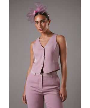Sleek tailored waistcoat with elegant V-neckline for a sophisticated silhouette
        Crafted from crepe fabric with a touch of stretch for comfortable all-day wear
        Structured design with button-through front detail for refined styling
        Clean-cut back with centre seam detailing for a polished finish
        Versatile cropped length perfect for coordinating with matching trousers or styling separately
    
    This tailored waistcoat from Coast offers the perfect blend of contemporary style and classic elegance. The structured silhouette creates a refined look whilst the V-neckline frames the dcolletage beautifully. Style as seen with the coordinating wide-leg trousers and a statement fascinator for race day sophistication, or pair with a crisp white shirt and tailored trousers for a modern take on formal dressing. For evening occasions, layer over a delicate camisole and team with a sleek midi skirt and strappy heels. The versatile design works wonderfully as part of a three-piece ensemble or as a standalone statement piece, making it an invaluable addition to your occasion wardrobe that will serve you for seasons to come.