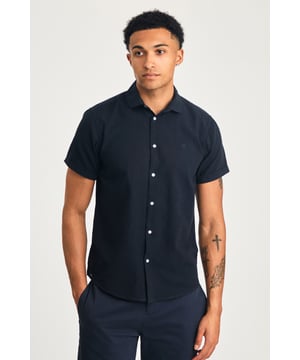This short sleeve cotton-linen mix shirt by Nines features a sleek embroidered logo on the chest. Lightweight and breathable, it’s perfect for warm days. A stylish and comfortable addition to your wardrobe, offering the ideal balance of relaxed yet refined style.