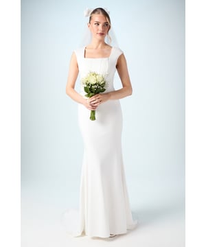 Elegant square neckline with structured cap sleeves for a sophisticated silhouette
        Streamlined ponte fabric that offers comfortable stretch while maintaining shape
        Striking fishtail design that creates a dramatic floor-sweeping effect
        Stunning puddle train detail for a truly memorable bridal entrance
        Figure-enhancing seam detailing that contours the body beautifully
    
    Make a breathtaking statement on your special day with this exquisitely designed wedding dress from Coast. The square neckline frames your dcolletage with timeless elegance, whilst the structured cap sleeves offer just the right amount of coverage. Crafted from ponte fabric that gently hugs your curves, this gown combines comfort with sophistication for all-day wearability. The fishtail silhouette gradually flares from the knee, culminating in a romantic puddle train that creates a stunning effect as you glide down the aisle. Complete your bridal look with a delicate veil as shown, pearl drop earrings and a simple bouquet of fresh blooms. For your reception, style with strappy heeled sandals and a subtle bracelet to maintain the gown's clean lines whilst allowing its architectural beauty to take centre stage.
