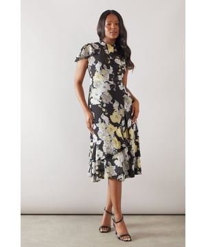 Elegant twist neck detail creates a sophisticated silhouette
        Feminine ruffle detailing on the short sleeves adds movement and charm
        Flattering maxi length with a graceful flared hem
        Striking floral print creates a standout look for special occasions
        Crew neckline offers a classic, refined finish
    
    This captivating Wallis maxi dress combines sophistication with feminine flair. The distinctive twist neck detail and delicate ruffle sleeves create a graceful silhouette that's perfect for formal events. The flowing maxi length with its subtle flare offers both comfort and elegance, whilst the eye-catching floral pattern ensures you'll make a memorable impression. Style with strappy heeled sandals as shown for weddings or race day events. For cooler evenings, layer with a tailored cropped jacket and add a clutch bag with minimal jewellery to maintain the dress as your focal point. This versatile piece transitions beautifully from daytime garden parties to evening celebrations, making it an essential addition to your occasion wardrobe.