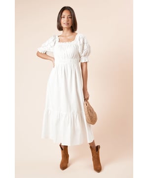 Elegant Bardot neckline with off-shoulder design for a feminine silhouette
        Delicate cutwork detailing on the sleeves adds a touch of artisanal charm
        Elasticated bodice creates a flattering gathered effect
        Tiered hem with a floaty finish for graceful movement
        Crafted from breathable cotton poplin for all-day comfort
    
    This charming Bardot dress combines effortless style with practical comfort. The off-shoulder design showcases your dcolletage beautifully, whilst the intricate cutwork detailing on the sleeves adds a distinctive touch to this otherwise understated piece. The elasticated bodice creates definition at the waist, flowing into a relaxed skirt with a tiered hem that moves gracefully as you walk. Style with western-inspired ankle boots as shown for casual brunches with the girls, or dress up with espadrille wedges for garden parties and family gatherings. The cotton construction ensures breathability, making this the perfect choice for warm-weather socialising. Layer with a denim jacket when the temperature drops for a look that transitions seamlessly from day to evening.