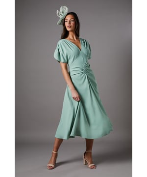 Elegant V-neckline with sophisticated ruched sleeve detail
        Flattering ruched waist design creating a feminine silhouette
        Flowing midi-length skirt with graceful movement
        Short sleeves with gentle volume for a contemporary touch
        Fully lined crepe fabric offering comfort and structure
    
    This exquisite midi dress from Coast embodies timeless elegance with its thoughtful design details. The ruched waist creates a figure-enhancing silhouette whilst the V-neckline frames the dcolletage beautifully. Perfect for weddings and race day events, style with strappy heels and a coordinating fascinator as shown for a sophisticated ensemble. The versatile midi length works wonderfully for formal garden parties or evening receptions. For cooler occasions, layer with a tailored blazer or delicate pashmina. Complete your look with statement earrings and a clutch bag for a polished finish that reflects the refined Coast aesthetic. The dress's graceful movement ensures you'll feel confident and poised throughout your special event.