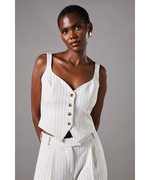 Elegant strappy waistcoat featuring a sophisticated pinstripe pattern
        Flattering V-neckline complemented by wide shoulder straps for comfort
        Decorative button-through front with contrasting metallic buttons
        Tailored fit with a slight stretch for a figure-enhancing silhouette
        Versatile cropped length perfect for pairing with high-waisted bottoms
    
    This refined Coast waistcoat brings contemporary sophistication to occasion dressing. The classic pinstripe pattern is reimagined with a feminine twist through the strappy design and fitted silhouette. Style with the matching wide-leg trousers as seen on our model for an impeccably coordinated ensemble that commands attention at summer weddings or race day events. For evening occasions, pair with a sleek pencil skirt and delicate jewellery for a look that conveys understated elegance. The crepe fabric offers comfortable wear throughout the day while maintaining its structured shape. This versatile piece transitions beautifully from formal daytime events to evening soires with just a change of accessories - try statement earrings and a clutch bag to transform your look as day turns to night.