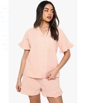 Classic gingham pattern throughout for a timeless nightwear aesthetic
        Charming ruffle detailing on both the short sleeves and shorts hems
        Relaxed button-up shirt with traditional collar for a smart-casual bedtime look
        Comfortable loose-fitting shorts with elasticated waist for ease of movement
        Coordinated two-piece set designed for mix-and-match versatility
    
    Drift into dreamland with this delightful gingham pyjama set from Boohoo. The playful ruffle details add a feminine touch to this classic nightwear ensemble, whilst the relaxed fit ensures maximum comfort for those cosy nights in. The traditional collar and button-up design lend a touch of sophistication to your evening routine. Perfect for lazy Sunday mornings with a cuppa and your favourite book, or for packing on weekend getaways when you want to feel put-together even at bedtime. The coordinated set works brilliantly as a complete look, but can also be paired separately with other nightwear favourites. For cooler evenings, simply layer with a soft dressing gown and fluffy slippers to complete your nighttime ensemble. This charming set embodies Boohoo's commitment to creating fashion that's both fun and functional for the style-conscious night owl.