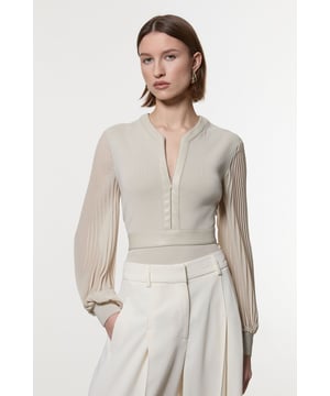 This Karen Millen top seamlessly blends sophistication with contemporary style. The knitted body offers a sleek fit, while the pleated woven sleeves add a touch of drama and movement. The faux leather trim along the V-neckline and waistband creates a striking contrast, enhancing the overall silhouette. Perfect for both day and evening wear, this top can be styled with tailored trousers and heels for a formal event, or paired with a pencil skirt for an office look. The versatility of this piece allows for endless styling possibilities, making it a valuable addition to any wardrobe. Whether you're attending a wedding, a cocktail party, or a business meeting, this top will ensure you look polished and fashion-forward.  Elegant V-neck design with faux leather trim Pleated woven sleeves for added texture Knitted body with a fitted silhouette Faux leather waistband for a defined shape Versatile piece suitable for various occasions