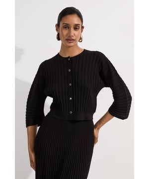 This Karen Millen Pleated Rib Summer Knit Cardigan combines sophisticated texture with relaxed elegance. The distinctive pleated ribbing creates a structured yet lightweight feel that's ideal for transitional weather. Style this versatile piece with the matching ribbed skirt for an effortlessly coordinated ensemble, or pair it with tailored trousers and flat sandals for casual daytime events. The three-quarter length sleeves and cropped silhouette make it perfect for family gatherings or weekend brunches. For cooler evenings, layer over a simple camisole and add statement earrings to enhance the look. This cardigan works beautifully with both neutral and bold accessories, allowing you to customise your outfit according to the occasion while maintaining a refined aesthetic that's quintessentially British.   Textured pleated rib design Three-quarter length sleeves with voluminous structure for a contemporary silhouette Button-through front closure Round neckline offers a flattering and timeless finish Cropped length perfect for high-waisted styling