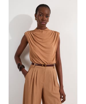 This versatile Karen Millen bodysuit combines contemporary design with everyday wearability. The high neck and artful ruching create a refined silhouette that works beautifully with both casual and smart-casual ensembles. Style with high-waisted trousers as shown for a polished daytime look, perfect for brunches or gallery visits. The sleek design pairs wonderfully with wide-leg jeans and trainers for weekend outings, or dress it up with a tailored blazer and statement jewellery for dinner dates. The bodysuit format eliminates the need for constant readjustment, making it an ideal foundation piece for busy days when comfort and style must work in harmony. Add a leather jacket and ankle boots to transition this piece effortlessly into evening drinks with friends.  Elegant high neck design with sophisticated ruched detailing for a flattering silhouette Sleeveless cut with gentle draping across the bodice for effortless style Bodysuit construction ensures a smooth, tucked-in finish that stays in place all day Soft jersey crepe fabric offers comfortable stretch and movement Stylish back opening with button fastening adds an unexpected design element