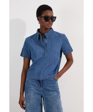 This Karen Millen denim shirt reimagines casual dressing with its contemporary half-button design and relaxed silhouette. The cropped length works brilliantly with high-waisted trousers, creating a balanced proportion that flatters the figure. This shirt can be styled with tailored linen trousers and leather sandals for a refined daytime look, or for cooler evenings layer it under a lightweight blazer. This versatile piece transitions seamlessly from casual coffee dates to informal garden parties, simply accessorise with statement sunglasses and delicate jewellery to customise your look for any occasion.   Relaxed fit denim shirt Classic collar detail with short sleeves Versatile cropped length perfect for high-waisted bottoms Metal button detailing adds subtle sophistication to this casual piece  Matching piece sold separately.