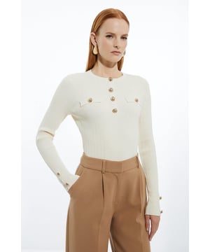 This Karen Millen Military Trim Rib Long Sleeve Knit Top is a versatile piece that seamlessly blends casual comfort with refined style. The ribbed knit fabric hugs your curves, creating a flattering silhouette that's perfect for various daytime occasions. Style it with high-waisted jeans and trainers for a relaxed weekend look, or pair it with tailored trousers and loafers for a smart-casual office ensemble. The gold-tone buttons add a touch of military-inspired sophistication, making this top an ideal choice for family gatherings or casual outings with friends. Layer it under a blazer for cooler days or wear it on its own when the weather permits. This top's versatility allows you to create multiple looks, making it a valuable addition to your wardrobe that can be dressed up or down with ease.   Ribbed knit texture for a sleek, form-fitting silhouette Military-inspired gold-tone buttons for a touch of elegance Long sleeves with button detailing at the cuffs Crew neckline for a classic, versatile look Slim fit design that accentuates the body's natural curves