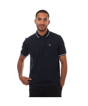 Mens Tommy Jeans Regular Fit Tipped Polo Shirt in navy.- Ribbed polo collar.- Two button placket.- Short sleeves with ribbed cuffs.- Contrast tipping at collar and cuffs- Embroidered Tommy Jeans flag patch at left chest.- Even vented hem.- Soft and comfortable cotton piqué fabric  made with at least 95% regenerative cotton.- Regular fit.- 100% Cotton.  Machine washable.- Ref: DM0DM20745C1G