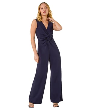 Dusk V-Neck Front Knot Jumpsuit from Roman. Be the epitome of chic in this knot jumpsuit, perfect for those warm Spring/Summer days. The flattering V-neck design with a stylish knot front detail creates a sophisticated look. This sleek sleeveless jumpsuit is a versatile piece that can be dressed up with strappy heels and a blazer for a night out or special occasion. Elevate your ensemble effortlessly and step out in style with this fashion-forward outfit!