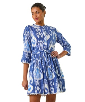 Tie Dye Buttoned Shirt Dress from Roman. Step out in style this Spring/Summer in this fun tie-dye knee length dress. Featuring a stand collar and long sleeves with charming buttons on the bodice, this dress is perfect for sunny days. The frilled skirt adds a flirty touch, while the tie-dye print adds a playful element to your look. Pair with sandals and stylish sunglasses for a chic and trendy outfit that's sure to turn heads wherever you go!