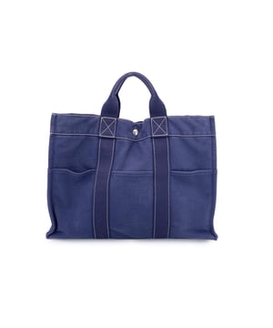 VINTAGE, RRP AS NEW
Hermès Paris Vintage Fourre Tout MM - A Timeless Everyday Classic  Step into the charm of effortless Parisian style with this vintage Hermès Fourre Tout MM tote, a beloved classic from the House of Hermès. Crafted in France from 100% cotton canvas, this tote radiates understated sophistication in a rich blue hue, accented by white contrast stitching that nods to traditional craftsmanship.  The Fourre Tout MM - meaning "carry-all" in French - lives up to its name with a clever, utilitarian design: three pockets on the front and three on the back, offering practical organization with a touch of vintage flair. Side snap buttons allow for expansion, making it as adaptable as it is stylish.  Its durable canvas handles make it a go-to for daily errands or leisurely weekends, while the open top with a central snap closure ensures quick access without sacrificing structure. Inside, you'll find a canvas-lined interior complete with a zip pocket featuring a leather zipper pull, a subtle nod to Hermès' fine leather heritage. An Hermès tag is stitched within - a quiet assurance of quality and legacy.  An icon of casual luxury, the Fourre Tout MM is not just a tote - it's a piece of Hermès history, perfectly suited for the modern vintage lover. Condition Rating: A - EXCELLENTCondition Details: Gently used. Some wear of use on bottom corners. Please check the photos carefully and ask if you need to know more details or if you have any doubts.Measurements (cm):Depth: 10.2Height: 30.5Length: 43.2Other Details: Dustbag? NoKeys? NoBox? No Measurments:  width: 102 mm length: 432 mm height: 305 mm