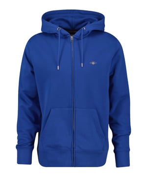 Diese Herren-Sweatjacke von Gant vereint Komfort und Stil in einem zeitlosen Design. Die Kapuze mit Tunnelzug sorgt für einen individuell anpassbaren Sitz. Der durchgehende Reißverschluss mit Kinnschutz ermöglicht einfaches An- und Ausziehen. Dank der hochwertigen Materialien bietet die Jacke ein angenehmes Tragegefühl den ganzen Tag über. Rippbündchen an Ärmeln und Saum sorgen für eine optimale Passform. Seitliche Eingrifftaschen bieten praktischen Stauraum für Kleinigkeiten. Das große Logo mit detailreichen Akzenten auf der Brust verleiht dem Design eine sportliche Note. Ein vielseitiges Must-have für jede Gelegenheit.