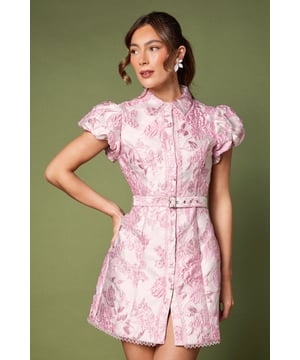 Exquisite jacquard fabric with textured floral pattern throughout
        Elegant collared neckline with front button fastening
        Feminine flutter sleeves with delicate volume
        Matching belt to define and flatter the waistline
        Mini length design perfect for showcasing statement footwear
    
    This striking jacquard mini dress presents a contemporary take on occasion wear. The structured silhouette features a smart collared neckline and decorative flutter sleeves that add a touch of romance to this sophisticated piece. The matching belt cinches the waist beautifully, creating a flattering hourglass shape that complements all figures. As shown, style with statement earrings and platform heels for race day elegance, or pair with refined court shoes and a clutch bag for wedding guest perfection. The textured fabric catches the light wonderfully, making this dress ideal for daytime events with a dress code. For cooler weather, layer with a tailored blazer or a delicate pashmina to maintain the refined aesthetic whilst ensuring comfort throughout your special occasion.