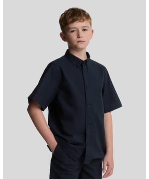 Breng tijdloze elegantie in hun voorjaarsgarderobe met het Linnen Korte Mouw Shirt. Licht en ademend, dit shirt is perfect voor warme dagen en smart-casual gelegenheden.\n\n- Premium Stof: Gemaakt van een linnen-katoenmix, wat zorgt voor zachtheid en ademend vermogen.\n- Klassiek Ontwerp: Voorzien van een knoopsluiting aan de voorkant met een subtiele, ontspannen kraag voor moeiteloze stijl.\n- Tonale Details: Versierd met een tonale geborduurde adelaar op de borst voor een ingetogen elegantie.\n- Veelzijdige Styling: Perfect te combineren met de Lyle & Scott linnen shorts of chinos voor een verzorgde, gecoördineerde look.\n\nDit korte mouw shirt is ideaal om kinderen comfortabel en stijlvol te houden, of het nu gaat om familie-uitjes of speciale evenementen in de lente- en zomermaanden.