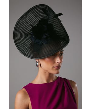 Statement fascinator with elegant flower detail for sophisticated occasion styling
        Structured wide brim design with distinctive ribbed texture
        Delicate feather embellishment creates a luxurious focal point
        Secure fit with discreet attachment for all-day comfort
        Dramatic silhouette perfect for formal events and special celebrations
    
    Make a striking impression at your next special event with this beautifully crafted Coast fascinator. The architectural wide-brimmed design creates a dramatic silhouette whilst the exquisite flower detail adds a touch of refined femininity. Style with an elegant dress in a bold jewel tone as shown for maximum impact at weddings or race day events. The structured shape frames the face beautifully, allowing you to showcase statement earrings for a coordinated finish. This versatile piece works wonderfully with both updos and sleek, straight styles, making it the perfect finishing touch for formal occasions. Pair with a tailored dress and classic court shoes for a sophisticated ensemble that reflects timeless British occasion dressing.