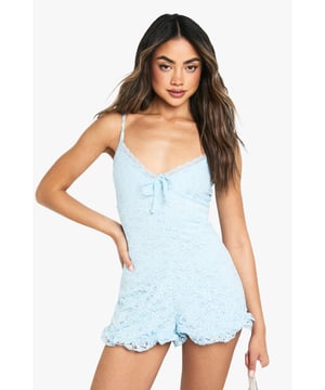 Delicate lace playsuit featuring a feminine ruffle hem detail
        Flattering strappy neckline with sweet bow accent at the centre
        Figure-hugging silhouette that showcases your shape
        Scalloped edges along the hem for an extra touch of charm
        Versatile design perfect for day-to-night styling
    
    This charming lace playsuit combines playful style with feminine details for a look that's both flirty and sophisticated. The delicate strappy neckline frames your dcolletage beautifully, while the ruffle hem adds movement and a touch of whimsy. Style with minimal flat sandals and a small handbag for casual daytime events as seen on our model, or transform for evening gatherings with statement earrings and strappy heels. The all-over lace texture creates visual interest without overwhelming your silhouette, making this playsuit ideal for family barbecues, brunches with friends, or relaxed garden parties. Layer with a denim jacket when the temperature drops for an effortlessly cool ensemble that maintains its casual charm whilst keeping you comfortable throughout the day.
