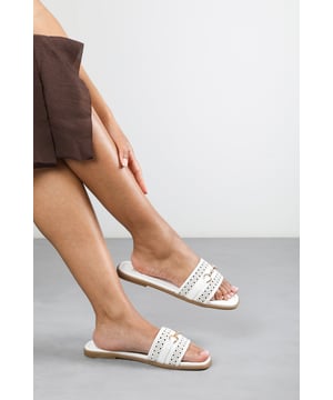 Step into timeless elegance with these Natalie Sliders With Geometric Strap And Metal Detail. Designed with a chic metallic horse-bit buckle, they effortlessly blend sophistication and comfort. The perforated upper adds breathable style, while the slip-on design makes them ideal for effortless wear from day to night. Perfect for holidays, casual brunches, or a polished everyday look. Key Features: • Material: Faux leather upper with a cushioned insole for all-day comfort • Design: Perforated detailing with a stylish horse-bit buckle accent • Closure: Easy slip-on style for convenience