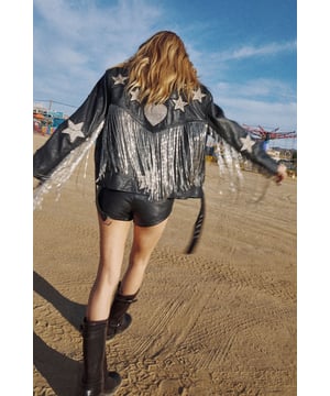 Genuine leather jacket featuring playful star and heart-shaped patches for distinctive character
        Statement metallic tassels cascade down the back for dramatic movement and flair
        Boxy, oversized silhouette offers a relaxed fit perfect for layering
        Classic biker-style design with notched lapels and asymmetric zip closure
        Fully lined interior ensures comfort and durability for long-lasting wear
    
    Make a bold statement with this eye-catching leather jacket from Nasty Gal. The oversized, boxy fit creates a contemporary silhouette that pairs brilliantly with both casual and evening looks. The striking tassel detail adds movement and drama to your ensemble, whilst the whimsical star and heart patches infuse a touch of playfulness into this edgy piece. Style with shorts and a crop top as shown for festival-ready vibes, or throw over a slip dress with chunky boots for an unforgettable night out look. Perfect for those who aren't afraid to stand out, this jacket works brilliantly for club nights, drinks with friends, or any urban adventure where you want to showcase your distinctive style. The versatile design allows for year-round wear - layer over knitwear during cooler months or drape over your shoulders on chilly summer evenings.