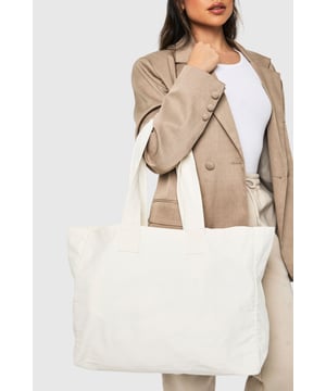 Spacious canvas tote bag with reinforced handles for durability
        Versatile rectangular design with a flat base for stability
        Minimalist aesthetic perfect for customisation with pins or patches
        Sturdy construction ideal for everyday use
        Generous capacity to accommodate all your essentials
    
    This essential canvas tote is the ultimate companion for the fashion-conscious woman on the go. The clean, unfussy design pairs effortlessly with any outfit, as demonstrated by our model who styles it with a tailored blazer and neutral trousers for a polished daytime look. Perfect for university lectures, weekend shopping trips or casual coffee dates, this bag offers both practicality and style in equal measure. The roomy interior easily accommodates your laptop, books, or gym kit, while the strong handles rest comfortably on your shoulder. For casual family gatherings, pair with relaxed denim and trainers, or take it to the beach as a chic alternative to traditional beach bags. This Boohoo tote represents versatility at its finest - a blank canvas that complements your personal style while keeping functionality at the forefront.