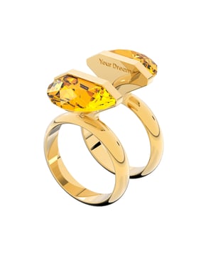 Expresa tu individualidad con este divertido anillo con motivo. Con un vibrante cristal de talla cuadrada en un animado tono amarillo, una pieza con un innovador cierre magnético y una doble banda bañada en tono oro. Llévalo solo o con otros diseños de la familia Lucent para realzar un look sencillo. Este anillo forma parte de la familia Lucent y ha sido diseñado por la directora creativa Giovanna Engelbert para la Collection II.\n Composición: Material:  Cristales, Baño tono oro, Imán\n Cuidados:\nEvite el contacto con cremas, perfumes y detergentes que puedan dañar el producto. Para mantener el brillo, le recomendamos limpiarlo solo con un paño suave.