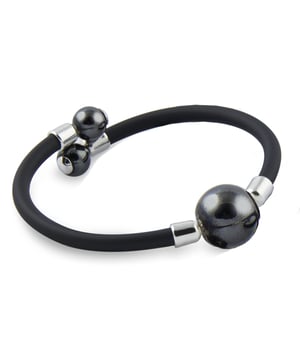 Black Pearl Bracelet from Mallorca Pearls: a modern contrast with an artisanal essence.\n\n A piece that fuses tradition and avant-garde, combining the elegance of the Mallorcan pearl with a contemporary rubber design. Ideal for those seeking a sober, contemporary style with a distinctive identity.\n\n Details:\n - Handcrafted in Mallorca using the traditional method.\n - Central Majorcan pearl, with a polished finish and uniform shine.\n - High quality rubber bracelet, flexible, durable and comfortable.\n - Metallic details at the ends.\n - Open design, easy to put on and adaptable to the wrist.\n\n An urban and elegant women's bracelet that adapts to both casual looks and more polished combinations. Perfect for those who value originality with artisanal roots.\n Measures: Diameter: 60 mm\n Composition: Eraser\n Care:\nAvoid contact with perfumes, creams and chemicals.