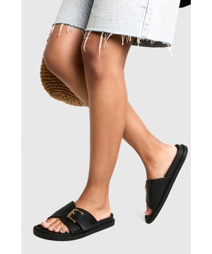 Sleek single-strap design with adjustable metal buckle detail
        Flat sole with comfortable 0-2cm heel height for all-day wear
        Smooth PU construction offering durability and easy maintenance
        Wide foot strap with contemporary minimalist aesthetic
        Slip-on style for effortless wearing and removal
    
    These versatile buckled sandals are the perfect addition to your casual wardrobe. The minimalist design pairs brilliantly with frayed denim as shown, but works equally well with floaty summer dresses or tailored shorts. The adjustable buckle ensures a customised fit while maintaining the clean, unfussy silhouette that makes these sandals so adaptable. Ideal for city breaks where comfort meets style, they'll take you from daytime sightseeing to casual evening meals without missing a beat. The flat profile offers stability for long walks, whilst the simple design ensures they'll complement virtually any outfit in your holiday collection. Perfect for family gatherings, weekend brunches or casual shopping trips when you need footwear that combines practicality with Boohoo's signature contemporary flair.