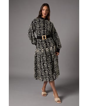 Exquisite lace fabrication with intricate pattern detailing throughout
        Elegant collared neckline with full button-through front design
        Voluminous long sleeves with defined cuffs for a dramatic silhouette
        Statement belt with oversized buckle to define the waist
        Midi length with a graceful tiered skirt for added movement
    
    This sophisticated shirt dress from Coast combines timeless elegance with contemporary flair. The striking lace pattern creates a captivating visual texture whilst the classic collared design maintains a refined sensibility. The dramatic full sleeves gather beautifully at the cuffs, creating a balanced proportion with the flowing tiered skirt. Style with strappy heeled sandals and a clutch bag for summer weddings or pair with elegant court shoes and a fascinator for race day events. For cooler occasions, layer with a tailored blazer in a complementary tone. The statement belt cinches the waist beautifully, creating a flattering hourglass silhouette that will command attention at any formal gathering. This versatile piece transitions effortlessly from daytime celebrations to evening receptions with just a change of accessories.