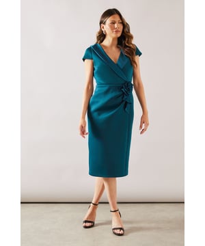 Elegant scuba midi dress with sophisticated wrap-effect bodice
        Flattering V-neckline frames the dcolletage beautifully
        Striking corsage detail at the waist adds a touch of glamour
        Figure-enhancing silhouette with a fitted bodice and straight skirt
        Short cap sleeves provide just the right amount of coverage
    
    The Wallis Scuba Corsage Midi Dress embodies sophisticated glamour for your special occasions. The wrap-effect bodice creates a flattering silhouette, whilst the V-neckline offers a feminine touch that's perfect for showcasing delicate jewellery. The standout corsage detail at the waist draws the eye and creates definition, complemented by the sleek midi-length skirt with a subtle back vent for ease of movement. Style with strappy heeled sandals as shown and a clutch bag for weddings or race day events. For cooler evenings, layer with a tailored blazer or an elegant pashmina. This versatile piece transitions beautifully from daytime ceremonies to evening receptions, ensuring you remain the epitome of sophistication throughout any formal occasion.