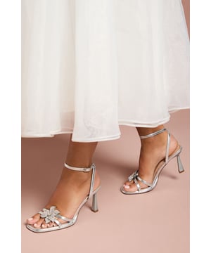 Elegant wide fit platform sandals featuring a stunning diamante corsage detail
        Adjustable ankle strap with secure buckle fastening for comfort and support
        Sophisticated high heel measuring between 7-9cm for an elegant lift
        Cushioned footbed designed for all-day comfort at special occasions
        Square-toe design with delicate strappy detailing for a contemporary finish
    
    The Taleesa high heel sandals from Coast combine show-stopping glamour with practical comfort. The striking diamante corsage adorning the front strap creates a luxurious focal point, whilst the wide fit design ensures these heels remain comfortable throughout your special event. Style these sophisticated sandals with a flowing maxi dress for summer weddings or pair with a tailored jumpsuit for race day elegance. The secure ankle strap provides stability whilst the platform element subtly balances the heel height, allowing you to dance the night away. Perfect for formal occasions where you wish to make an impression without compromising on comfort, these versatile heels will become your go-to choice for celebrations and milestone events throughout the season.