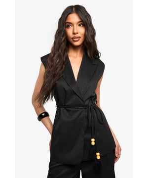 Sleeveless wrap waistcoat with sophisticated lapel detailing
        Flattering loose fit design for effortless movement
        Stylish belt with decorative wooden bead accents
        Linen-look texture adding dimension to your outfit
        Versatile layering piece suitable for multiple seasons
    
    This chic waistcoat combines contemporary styling with timeless appeal. The wrap design creates a flattering silhouette while the loose fit ensures comfort for all-day wear. Style with the coordinating wide-leg trousers as seen on our model for a polished co-ord look that's perfect for casual gatherings. For daytime outings, pair with your favourite denim and trainers, adding statement sunglasses for a touch of glamour. When evening approaches, transform your look by layering over a fitted top and accessorising with a structured handbag. The belt with wooden bead detailing adds a distinctive finishing touch that draws the eye and defines the waist. This versatile piece transitions seamlessly from family brunches to casual meetups, embodying boohoo's commitment to inclusive, trend-focused fashion that works for every occasion.
