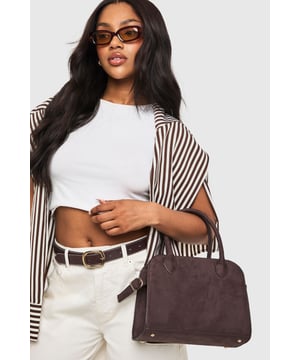 Classic bowling bag silhouette with structured design for a timeless appeal
        Faux suede finish with a soft-touch texture that adds sophistication
        Dual top handles with reinforced stitching for comfortable carrying
        Detachable shoulder strap with gold-tone hardware for versatile styling options
        Spacious interior with secure fastening to keep your essentials organised
    
    The Wildleder Bowling-Tasche from Boohoo combines retro charm with contemporary practicality. This structured bag presents a versatile addition to your accessory collection, perfect for those who appreciate both style and function. Pair with casual daywear as seen on our model - try white trousers and a cropped top with an oversized striped shirt for an effortlessly chic weekend look. The bag's classic shape works brilliantly for family gatherings or brunches with friends, while the detachable strap offers multiple carrying options to suit your mood. The faux suede texture adds a touch of luxury to everyday outfits without compromising on durability. Whether you're running errands or meeting friends for coffee, this bowling bag offers the perfect balance of fashion-forward design and practical storage for all your daily essentials.