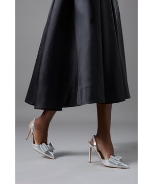 Striking metallic textile court shoes featuring an elegant satin bow detail at the pointed toe
        Sophisticated slingback design with adjustable strap for the perfect fit
        Sleek high stiletto heel measuring between 7-9cm for a graceful silhouette
        Pointed toe shape creates a flattering, elongated look for the foot
        Versatile design suitable for formal occasions whilst maintaining all-day comfort
    
    The Tamara Metallic Textile Slingback Heels present the perfect marriage of sophistication and contemporary style. The striking satin bow adorning the pointed toe creates a feminine focal point, whilst the slingback design offers both security and elegance. These court shoes feature a beautifully balanced high stiletto heel that provides a confident stance without compromising on comfort. Style these versatile heels with a flowing midi dress for summer weddings, or pair with tailored trousers and a silk blouse for race day elegance. The metallic finish catches the light beautifully as you move, making these shoes ideal for special occasions where you wish to make a refined statement. Their timeless design ensures they'll remain a treasured addition to your wardrobe for countless formal events, from graduation ceremonies to elegant evening affairs.