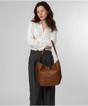 Handcrafted from natural leather with a soft to the touch finish, the 'Sofia' tote bag from NiNa Amora is a must-have thanks to its attractive metal fittings and zips. The main compartment is secured with a magnetic press stud and complemented by a leather strap which drapes over the top. Inside the spacious design is a zipped divider compartment alongside ample space for your essentials which is complemented by slip and zip pockets on the interior which are perfect for your keys, phone and any other day to day accessories. This style is adorned with a single leather handle with a drop length of 35cm. This is finished with the NiNa Amora X logo embossed in silver foil on the front and hanging charm for a luxurious and elegant touch.