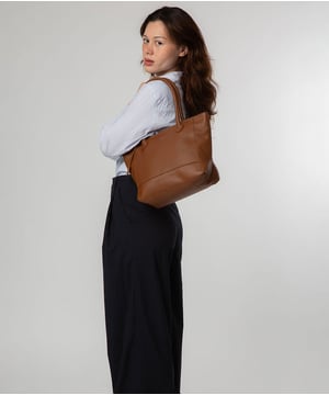As part of the NiNa Amora brand, the 'Margarida' tote bag is inspired by our designer's daughter and all about elevating classic designs with high quality leather. A concealed zip-over top secures the spacious main lined compartment which opens to reveal additional storage space in the form of a slip and zipped pocket; ideal for your phone, keys and any other essentials. The classic angular sides of the tote are updated with this sophisticated design and adorned with slim leather handles with a drop length of 20cm. This bag is finished with sophisticated silver metal fittings and zips which are complemented by the NiNa Amora X logo embossed in silver on the front and on the hanging charm. Effortlessly chic.