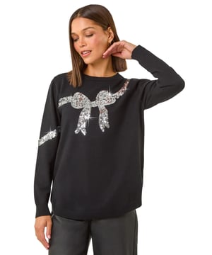 Bow Sequin Detail Knit Jumper from Roman. Add a touch of sparkle to your Autumn Winter wardrobe with our charming sequin bow detail jumper. The classic crew neckline and long drop-shoulder sleeves make this knitted jumper cosy and stylish for the chilly days ahead. Crafted from a mix of knitted fabrics, this embellished piece is both fashionable and comfortable. For a trendy fall look, pair with jeggings and ankle boots to add a touch of glamour to your outfit!