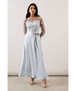 Elegant maxi dress featuring delicate mesh overlay with intricate embroidered detailing
        Sophisticated crew neckline and three-quarter length sheer sleeves for refined coverage
        Flattering satin skirt that flows gracefully to a maxi length
        Feminine waist tie belt to accentuate your silhouette
        Stunning illusion effect created by the contrast between the mesh bodice and lined underskirt
    
    This enchanting Wallis occasion dress combines the luxurious feel of satin with the delicate beauty of embroidered mesh for a truly sophisticated ensemble. The sheer overlay across the bodice and sleeves creates a captivating illusion effect, whilst the flowing maxi skirt offers graceful movement as you walk. Perfect for weddings, formal dinners or race day events, this dress radiates timeless elegance. Style with metallic strappy heels and a coordinating clutch for classic sophistication. For cooler evenings, layer with a tailored cropped jacket or elegant pashmina. Complete your look with understated jewellery, such as the delicate drop earrings shown, to maintain the dress's refined aesthetic whilst allowing the exquisite embroidery detail to remain the focal point of your ensemble.