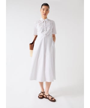 This Grace dress is a timeless piece in white cotton poplin, featuring an embroidered lace bib panel, self-covered ball buttons, and pockets. It offers a sophisticated yet playful aura, ideal for smart casual events like garden parties or brunch outings. Pair it with strappy sandals or stylish ankle boots for a look that turns heads.