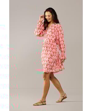 De elegante Belfast print tuniek uit de nieuwste collectie van Caroline Tensen is dé ideale keuze voor de zomer. De soepelvallende, wijde pasvorm en verfijnde details geven de tuniek zowel een chique als een ontspannen uitstraling. Het opvallende oranje pauwenprint op een zachte koraalroze achtergrond maakt deze lange tuniek bijzonder uniek. De lange mouwen hebben een subtiel ballon-effect en eindigen in speelse ruches bij de polsen, afgewerkt met elastiek voor extra comfort. De tuniek heeft een V-hals met een opengewerkte bies en een recht silhouet, waardoor hij heerlijk comfortabel zit. Dankzij het vaste strikceintuur kun je de taille mooi benadrukk